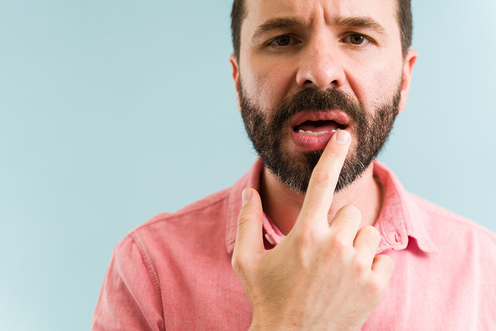 Attractive man touching his mouth and feeling a little pain because of his dry lips. Close up of a latin man applying lip balm